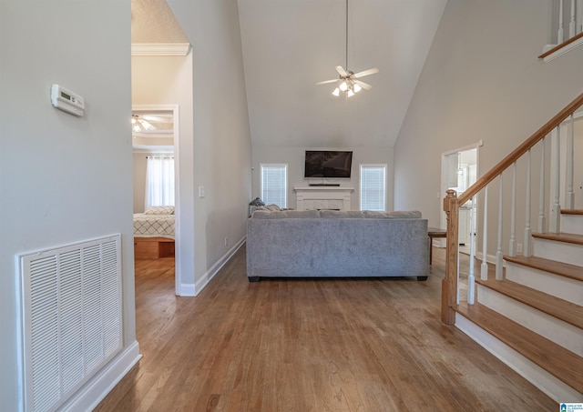 unfurnished living room featuring visible vents, a ceiling fan, wood finished floors, high vaulted ceiling, and stairs