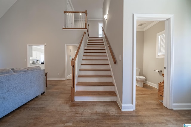 staircase featuring crown molding, a towering ceiling, baseboards, and wood finished floors