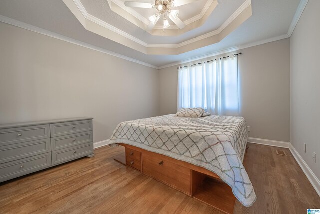 bedroom with ceiling fan, baseboards, ornamental molding, a tray ceiling, and light wood finished floors