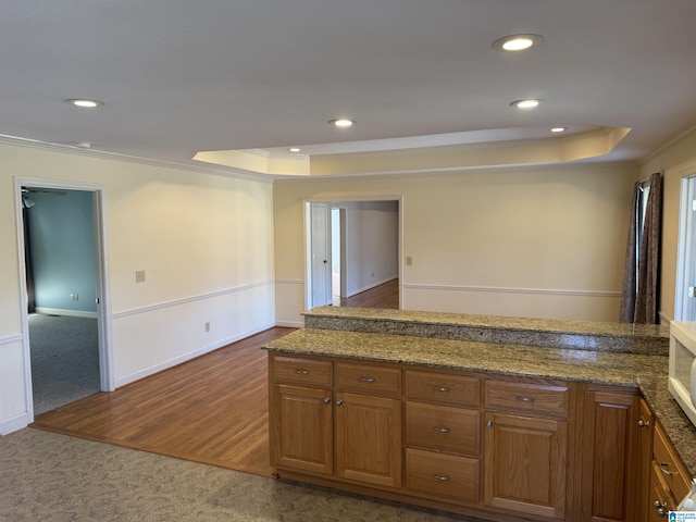 kitchen featuring brown cabinetry, dark carpet, a raised ceiling, and crown molding