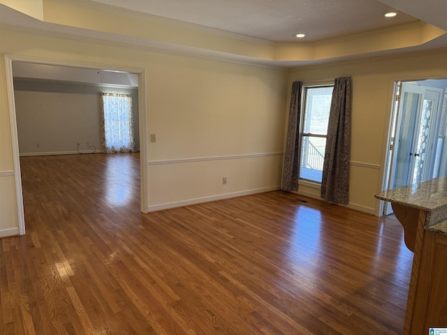 empty room featuring a tray ceiling, crown molding, baseboards, and wood finished floors