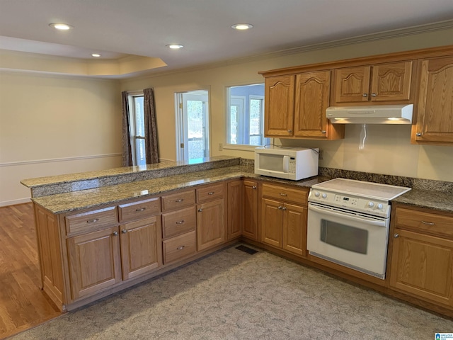 kitchen featuring white appliances, brown cabinetry, dark stone countertops, a peninsula, and under cabinet range hood