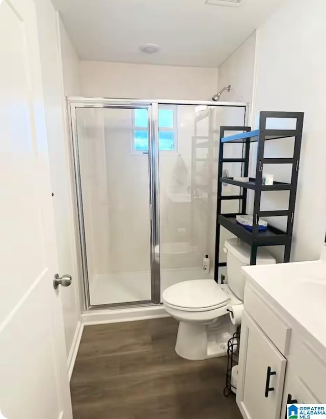 bathroom with visible vents, toilet, wood finished floors, vanity, and a shower stall