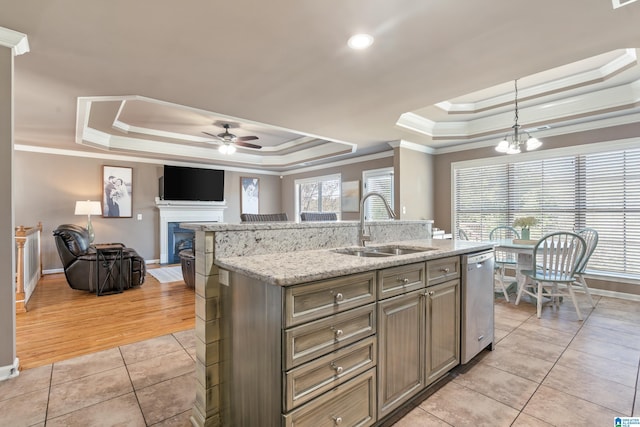 kitchen with open floor plan, a tray ceiling, stainless steel dishwasher, a sink, and light tile patterned flooring