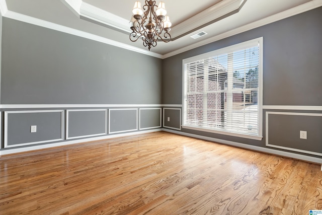 spare room featuring a chandelier, wood finished floors, visible vents, ornamental molding, and a raised ceiling