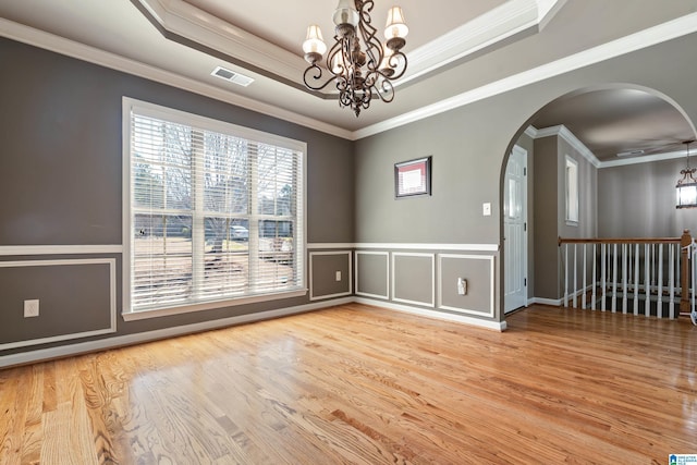 unfurnished room featuring visible vents, arched walkways, wood finished floors, a tray ceiling, and a notable chandelier