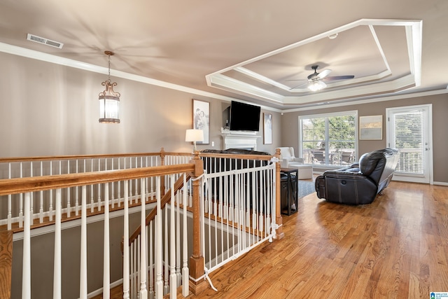 interior space featuring a tray ceiling, visible vents, ornamental molding, an upstairs landing, and wood finished floors