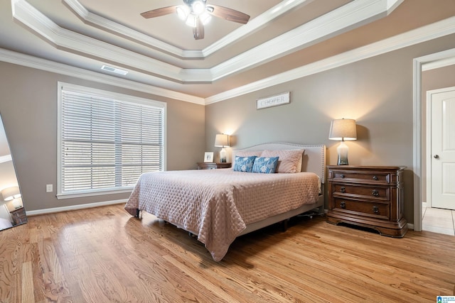 bedroom with light wood-type flooring, a raised ceiling, visible vents, and crown molding