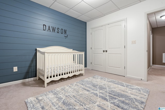 carpeted bedroom featuring a paneled ceiling, wood walls, baseboards, a closet, and a crib