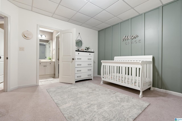 bedroom with carpet floors, a nursery area, a drop ceiling, and a decorative wall