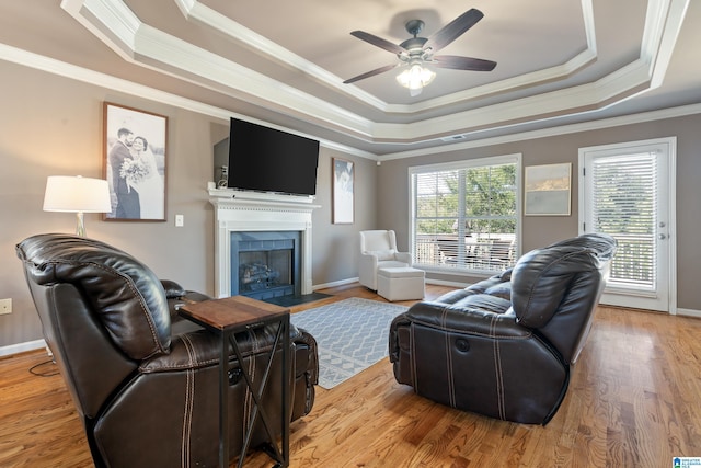 living area with a fireplace with flush hearth, wood finished floors, baseboards, a raised ceiling, and crown molding