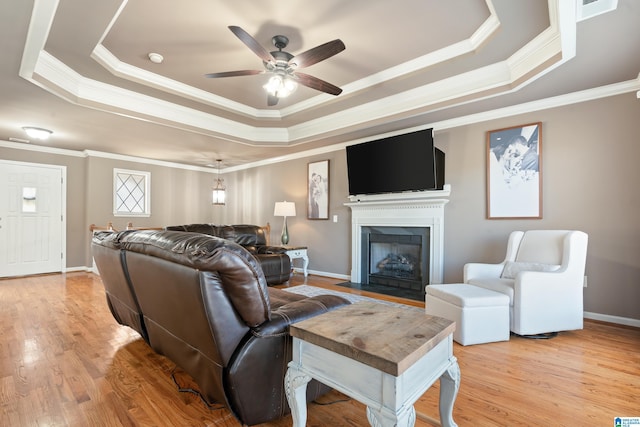 living area featuring a fireplace with flush hearth, baseboards, light wood-style floors, a tray ceiling, and crown molding