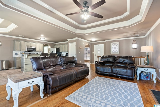 living area with ornamental molding, a tray ceiling, arched walkways, and light wood-style floors