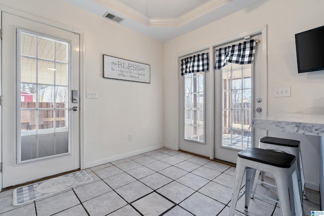 doorway with light tile patterned floors, visible vents, baseboards, a raised ceiling, and crown molding