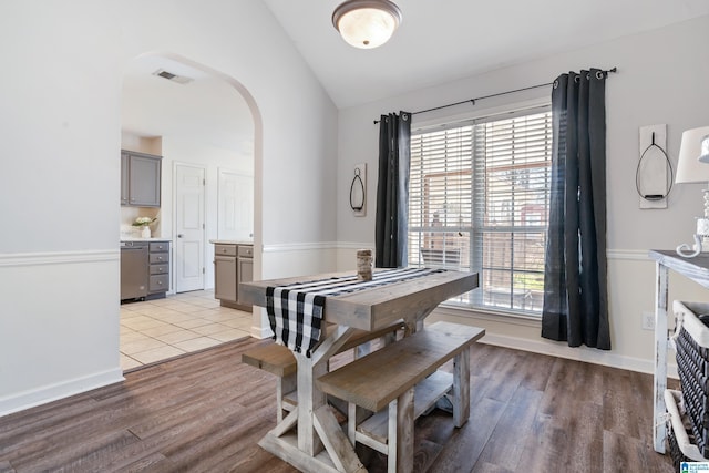 dining room featuring arched walkways, light wood-style flooring, vaulted ceiling, and visible vents