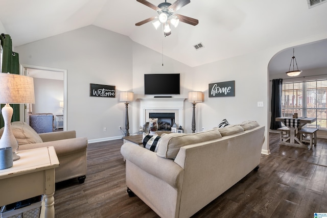 living area featuring arched walkways, ceiling fan, dark wood-style flooring, vaulted ceiling, and a fireplace