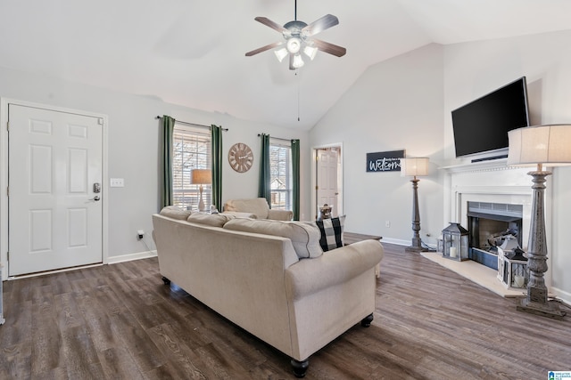 living area with ceiling fan, baseboards, a fireplace with raised hearth, and dark wood-style flooring