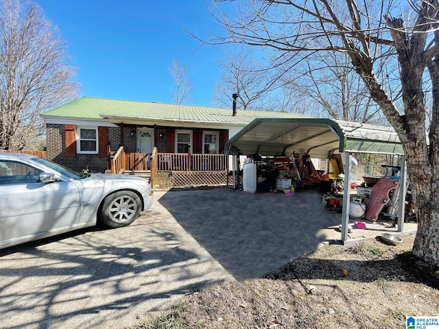 view of front of house with brick siding, a detached carport, covered porch, metal roof, and driveway