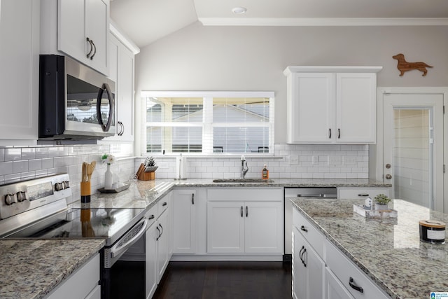 kitchen featuring white cabinets, decorative backsplash, appliances with stainless steel finishes, vaulted ceiling, and a sink