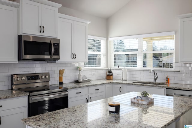 kitchen featuring appliances with stainless steel finishes, vaulted ceiling, white cabinetry, and a sink