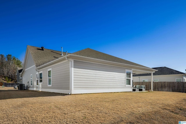 view of side of property featuring a shingled roof, central AC, fence, and a lawn