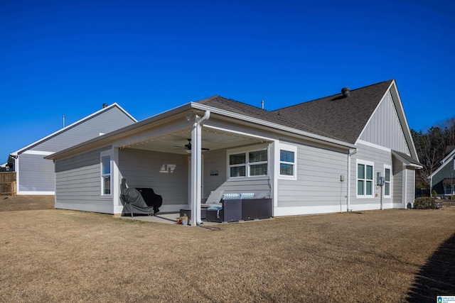 rear view of property with a lawn, ceiling fan, roof with shingles, a patio area, and board and batten siding