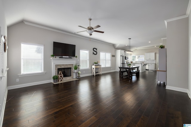 living area with baseboards, a ceiling fan, dark wood-style flooring, crown molding, and a stone fireplace