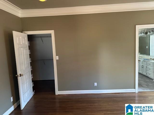 unfurnished bedroom with a walk in closet, a closet, crown molding, and wood finished floors