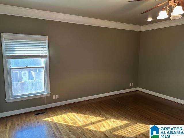 spare room featuring baseboards, wood finished floors, visible vents, and crown molding