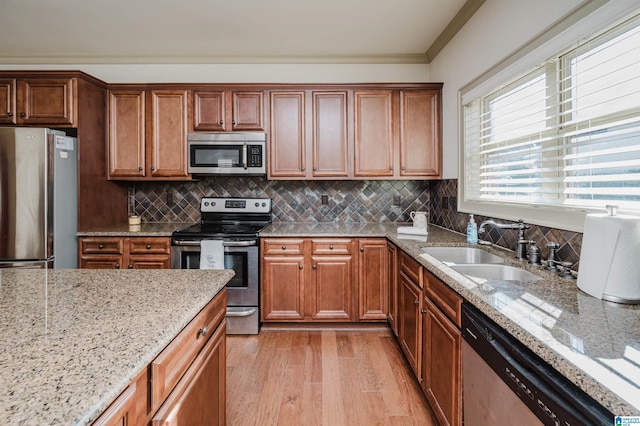 kitchen featuring a sink, light wood-style floors, appliances with stainless steel finishes, light stone countertops, and tasteful backsplash