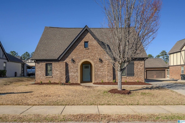 english style home featuring a garage, roof with shingles, and brick siding