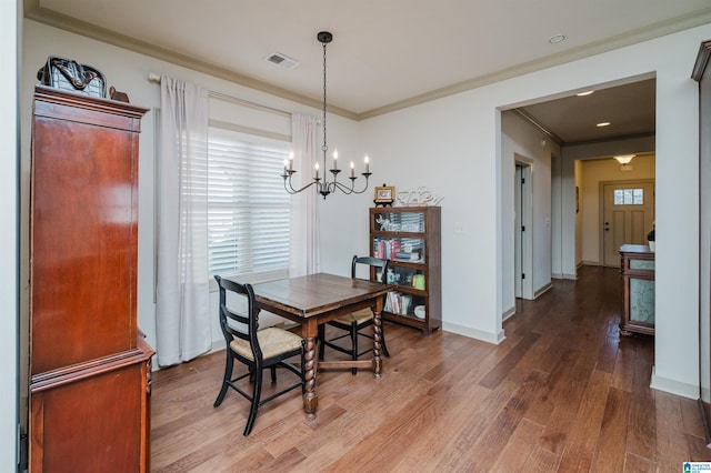 dining space with crown molding, visible vents, an inviting chandelier, wood finished floors, and baseboards