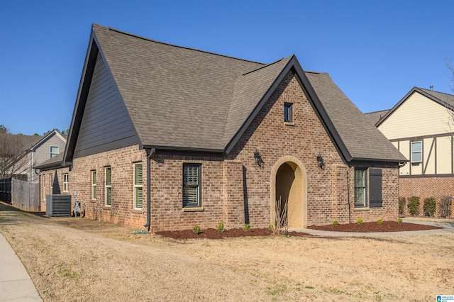 english style home with central air condition unit, a shingled roof, and brick siding