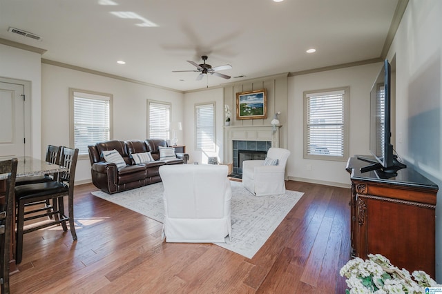 living room featuring ornamental molding, a tile fireplace, dark wood-style flooring, and visible vents