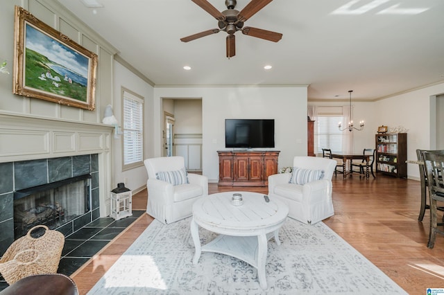 living area featuring recessed lighting, ceiling fan with notable chandelier, a fireplace, wood finished floors, and crown molding