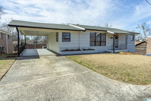 single story home with concrete driveway, an attached carport, a front yard, and a shingled roof