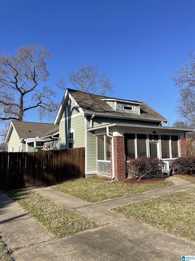 view of front of home featuring a front yard, a sunroom, brick siding, and fence