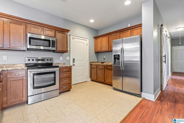 kitchen featuring recessed lighting, stainless steel appliances, baseboards, brown cabinets, and light stone countertops