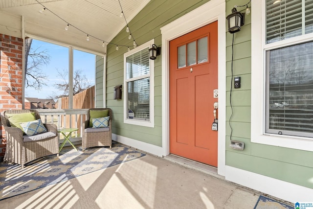 view of exterior entry featuring covered porch and fence