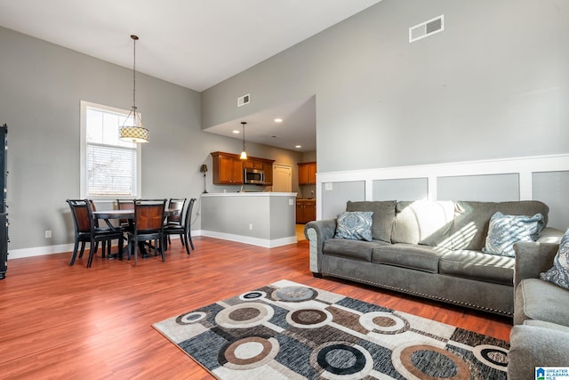 living area featuring a towering ceiling, baseboards, visible vents, and wood finished floors