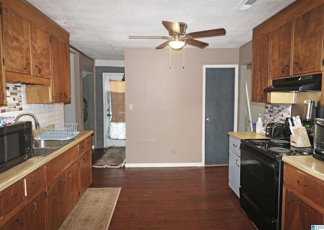 kitchen with dark wood finished floors, light countertops, black appliances, under cabinet range hood, and baseboards