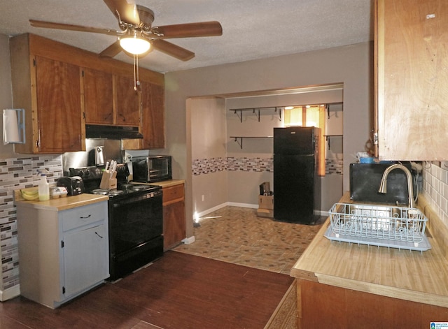 kitchen featuring black appliances, tasteful backsplash, under cabinet range hood, and light countertops