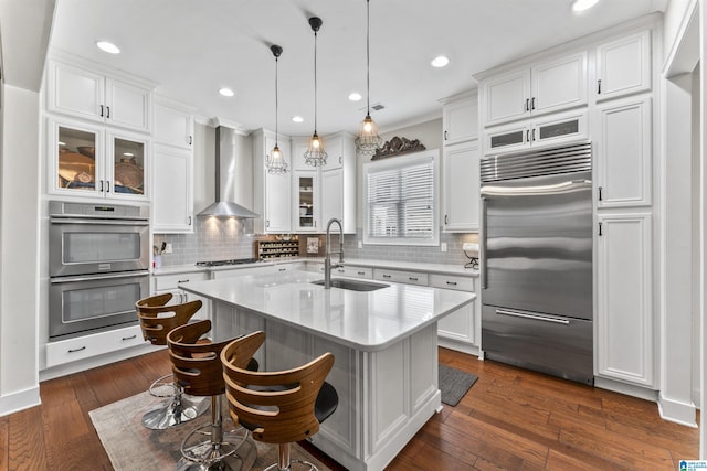 kitchen featuring stainless steel appliances, a sink, white cabinetry, wall chimney range hood, and dark wood-style floors