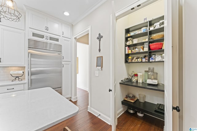 kitchen with built in refrigerator, white cabinetry, dark wood finished floors, and decorative backsplash