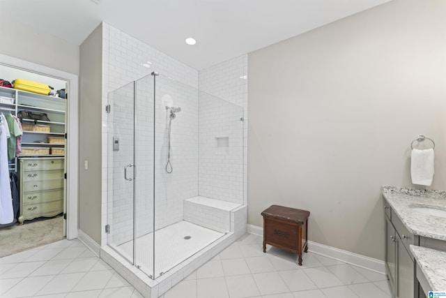 full bath with a spacious closet, a shower stall, vanity, tile patterned flooring, and baseboards