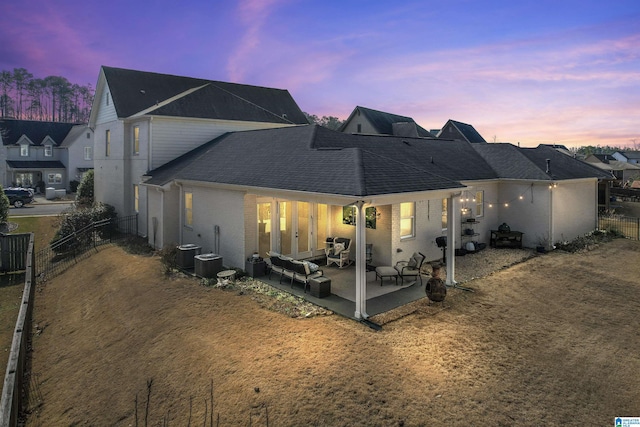 back of property at dusk with roof with shingles, brick siding, a patio, and fence