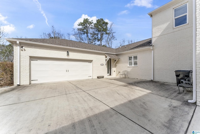 exterior space featuring a garage, concrete driveway, brick siding, and roof with shingles