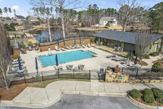 pool with an outbuilding, a patio, a water view, a gate, and fence