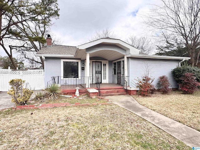 bungalow with a chimney, roof with shingles, covered porch, fence, and a front yard