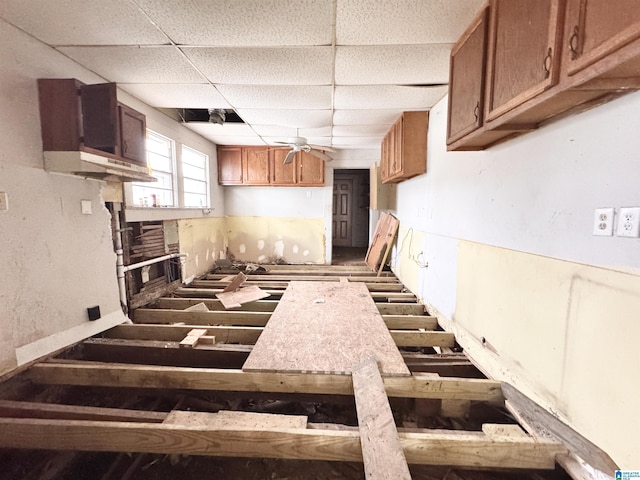 kitchen with a ceiling fan, brown cabinetry, and a drop ceiling